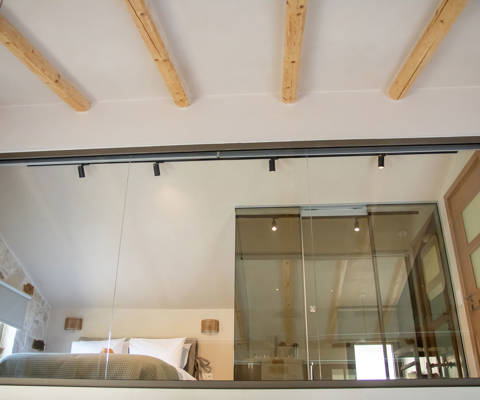 Modern loft-style bedroom with exposed wooden beams, glass wall and cozy decor