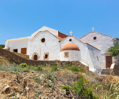 Traditional whitewashed church with multiple domes and crosses under a clear blue sky in Crete