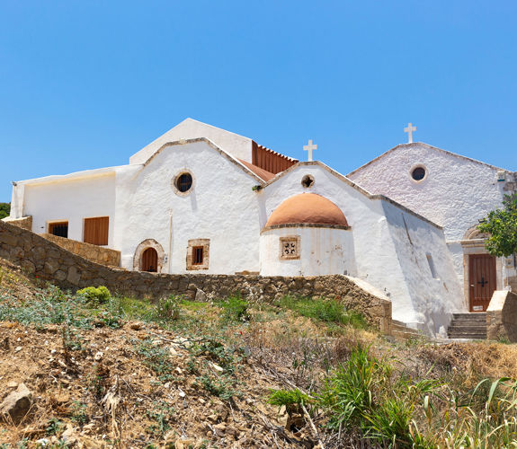 Traditional whitewashed church with multiple domes and crosses under a clear blue sky in Crete