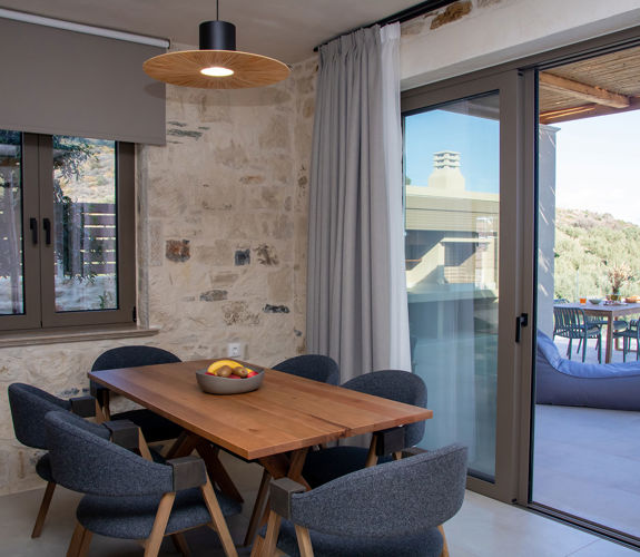 Dining area with wooden table and chairs, stone walls and large balcony doors leading to outdoor seating