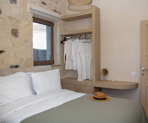 Bedroom interior with double bed under a window, stand with hangers, and office space next to the door