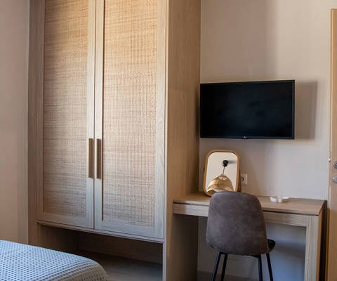Bedroom with two single beds, wooden wardrobe, desk with chair and wall-mounted TV.