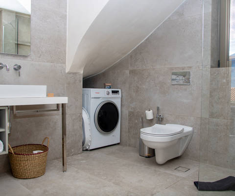 Spacious bathroom interior with laundry area, glass-enclosed shower, large sink with mirror, basket for laundry and space with folded towels