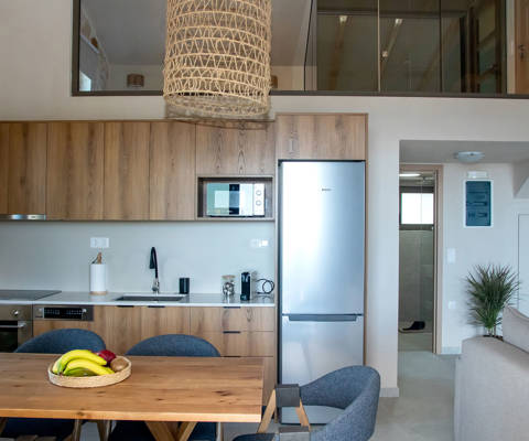 Modern open-plan kitchen with wooden cabinets, dining table with chairs and view of the loft bedroom above