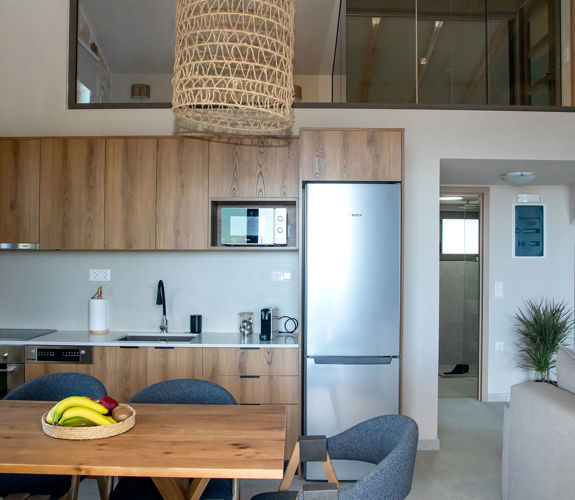 Modern open-plan kitchen with wooden cabinets, dining table with chairs and view of the loft bedroom above