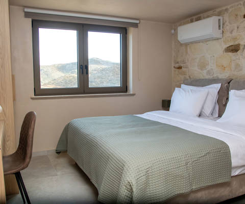 Cozy bedroom with double bed, stone accent wall, air-conditioning, desk and large window with a view.