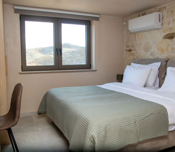 Cozy bedroom with double bed, stone accent wall, air-conditioning, desk and large window with a view.