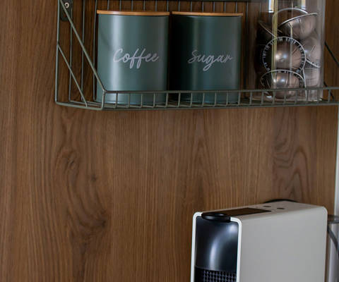 Coffee station with espresso machine, coffee and sugar containers, and a capsule holder on a wooden wall.