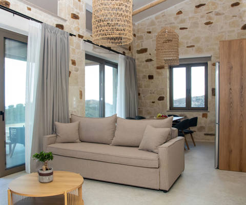 Bright living area with sofa, stone walls, large windows and balcony doors with access to the outdoor terrace