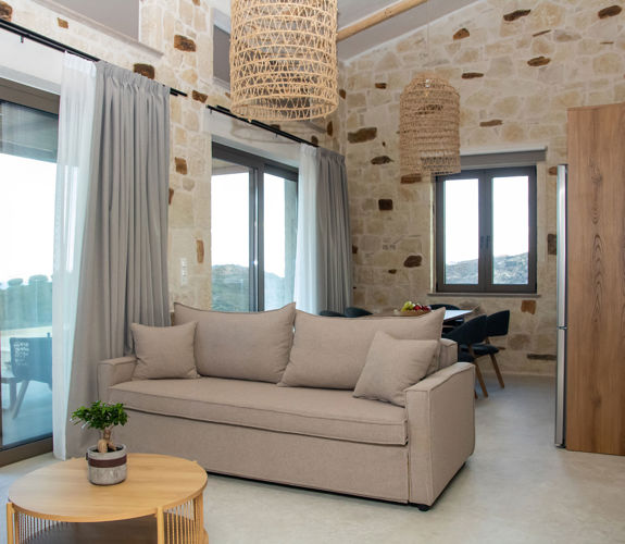 Bright living area with sofa, stone walls, large windows and balcony doors with access to the outdoor terrace