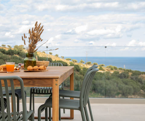 Outdoor dining table with breakfast setup, overlooking olive groves and the sea