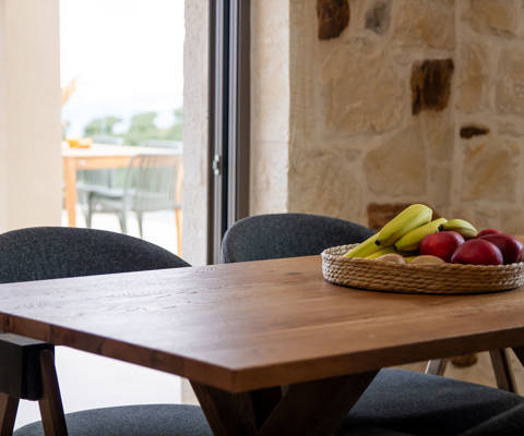 Wooden dining table with fruit basket next  to balcony door leading to outdoor seating area