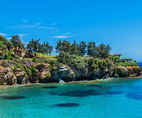 Rocky coastline with turquoise waters in Agia Pelagia, Crete, under a clear blue sky.