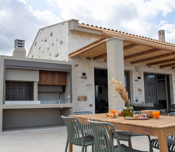 Outdoor dining area with breakfast setup, barbecue station and view of a beautiful stone villa