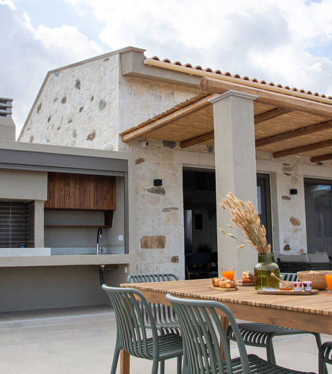 Outdoor dining area with breakfast setup, barbecue station and view of a beautiful stone villa