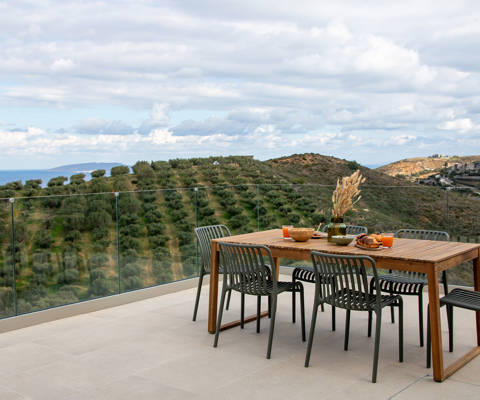 Outdoor dining area with panoramic view of olive groves and the sea.