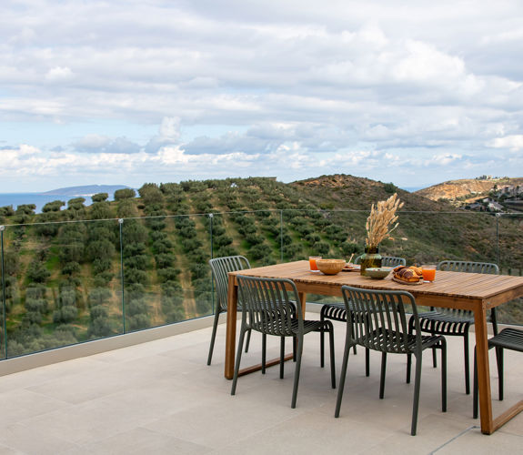 Outdoor dining area with panoramic view of olive groves and the sea.