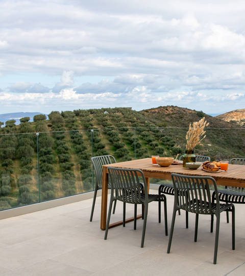 Outdoor dining area with panoramic view of olive groves and the sea.